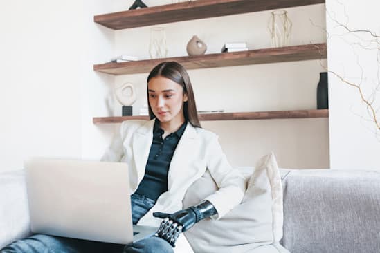Smarte Frau sitzt auf dem Sofa am Labtop mit Armprothese. Smarte Frau sitzt auf dem Sofa am Labtop mit Armprothese.