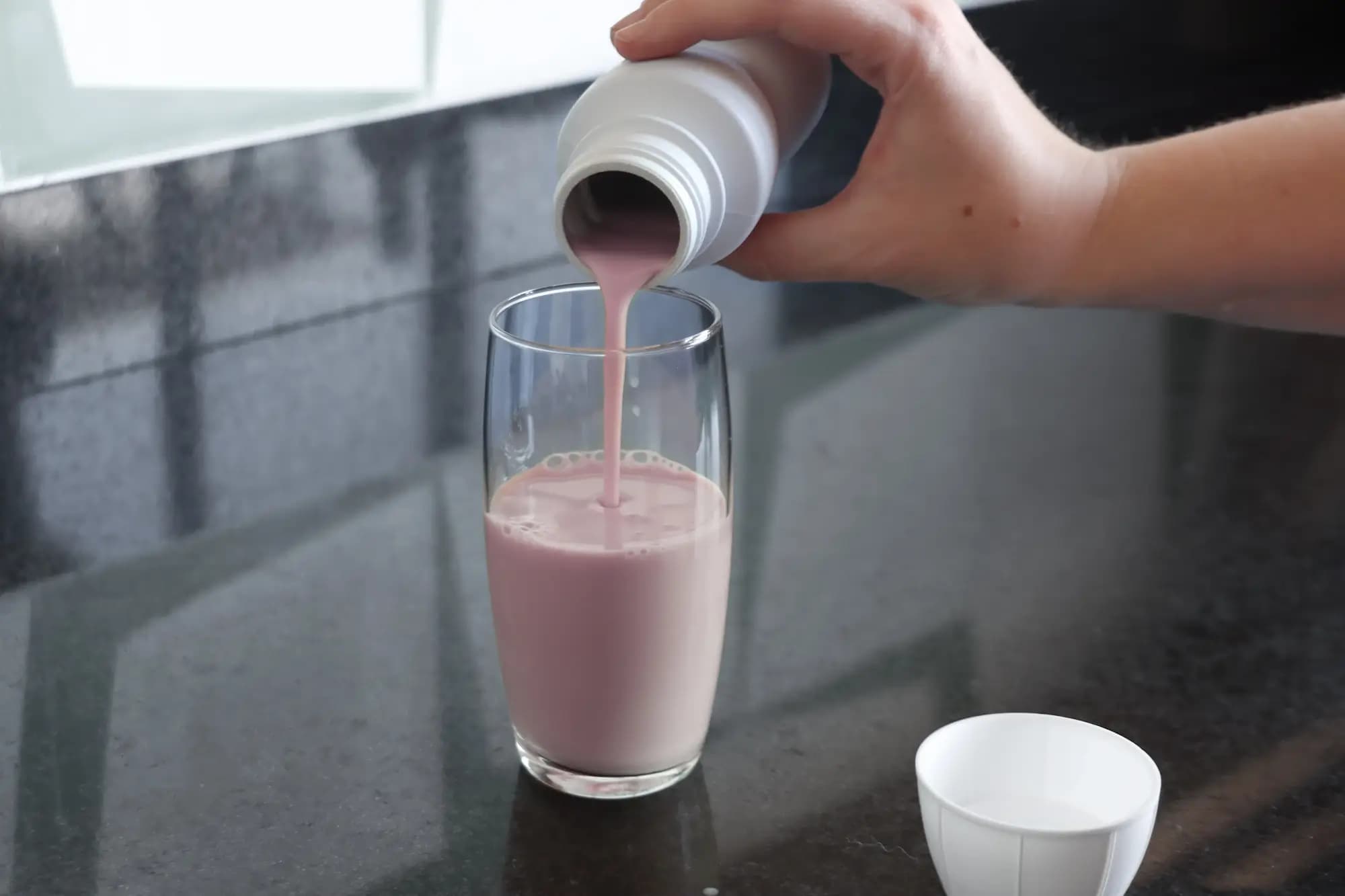 Hand kippt kleinen Fitnessshake aus einer kleinen Flasche in ein Glas Hand kippt kleinen Fitnessshake aus einer kleinen Flasche in ein Glas