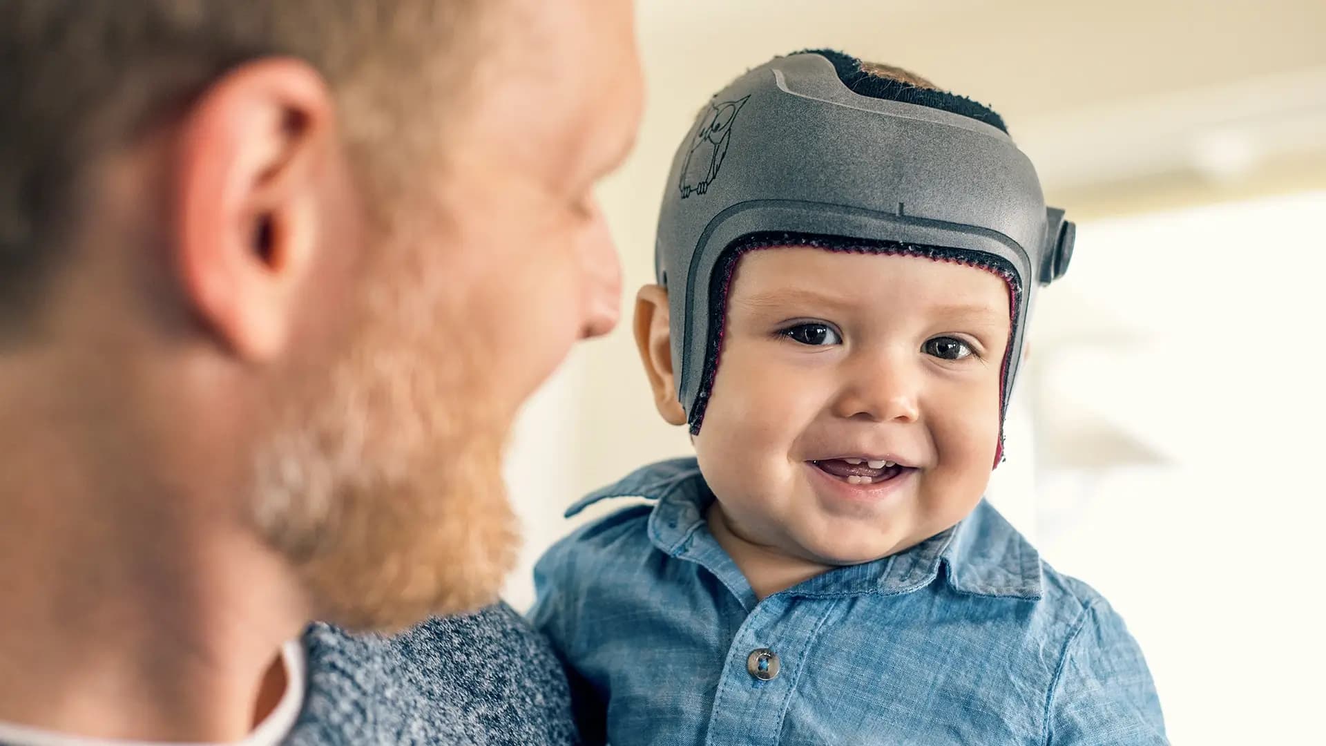 Kind wird von Vater auf Arm getragen und trägt Kopfschutzhelm Kind wird von Vater auf Arm getragen und trägt Kopfschutzhelm