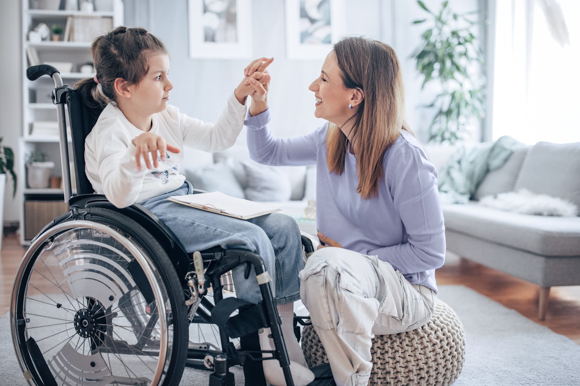 Mutter knied vor ihrem Kind im Rollstuhl und hält seine Hand. Mutter knied vor ihrem Kind im Rollstuhl und hält seine Hand.