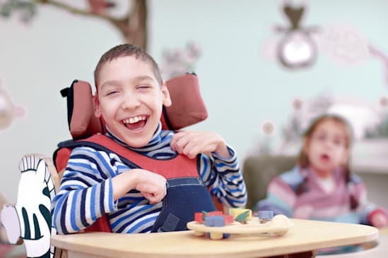 Kind sitzt mit Sitzschale unterstützt zum spielen an einem Tisch. Kind sitzt mit Sitzschale unterstützt zum spielen an einem Tisch.