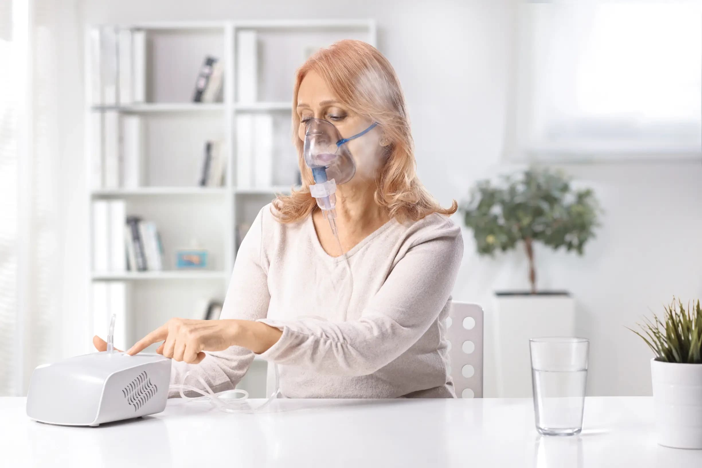 Patientin sitzt am Tisch und nutzt Inhalationsgerät Patientin sitzt am Tisch und nutzt Inhalationsgerät