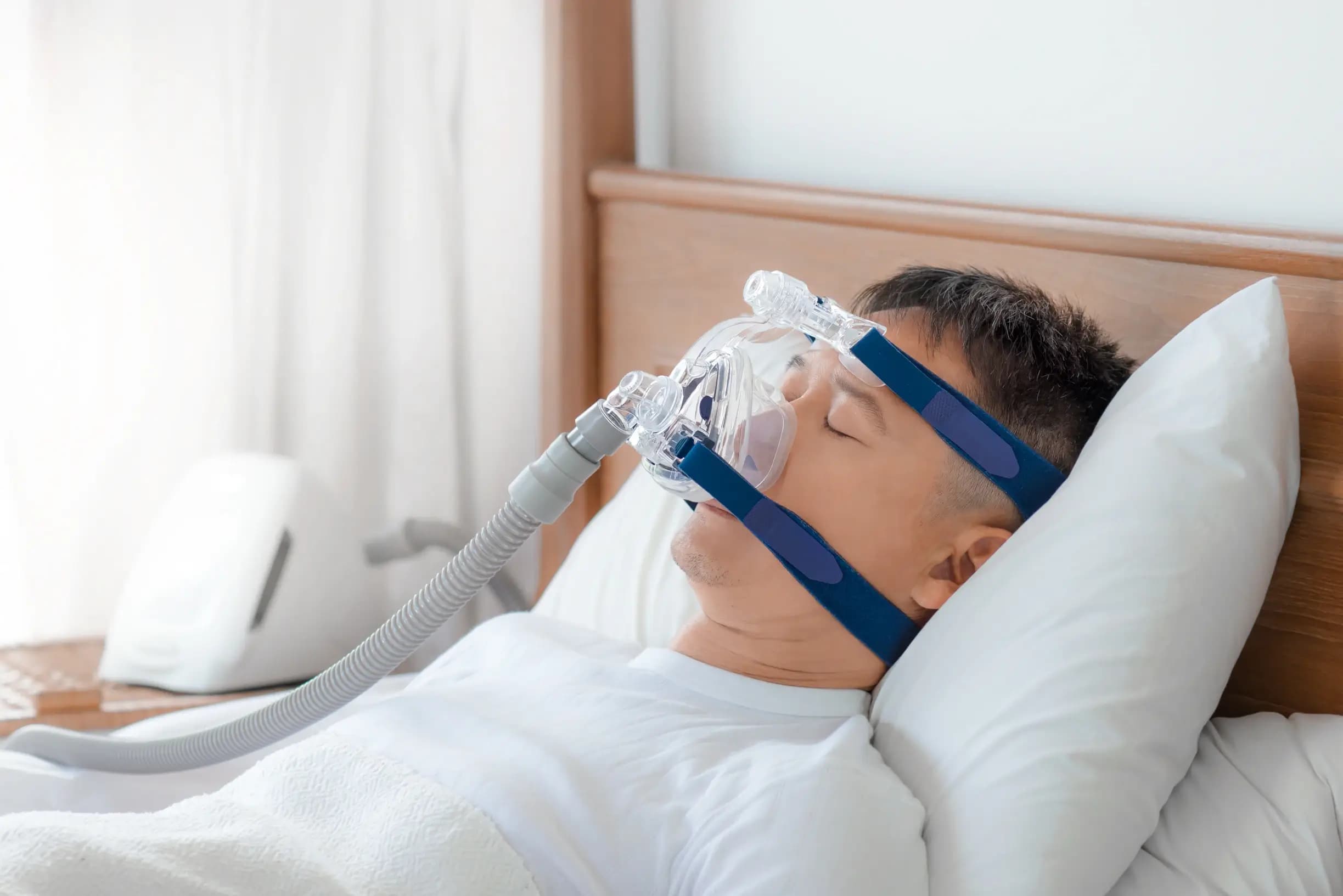 Männlicher Patient liegt im Krankenhausbett, schläft und wird nicht-invasiv beatmet Männlicher Patient liegt im Krankenhausbett, schläft und wird nicht-invasiv beatmet