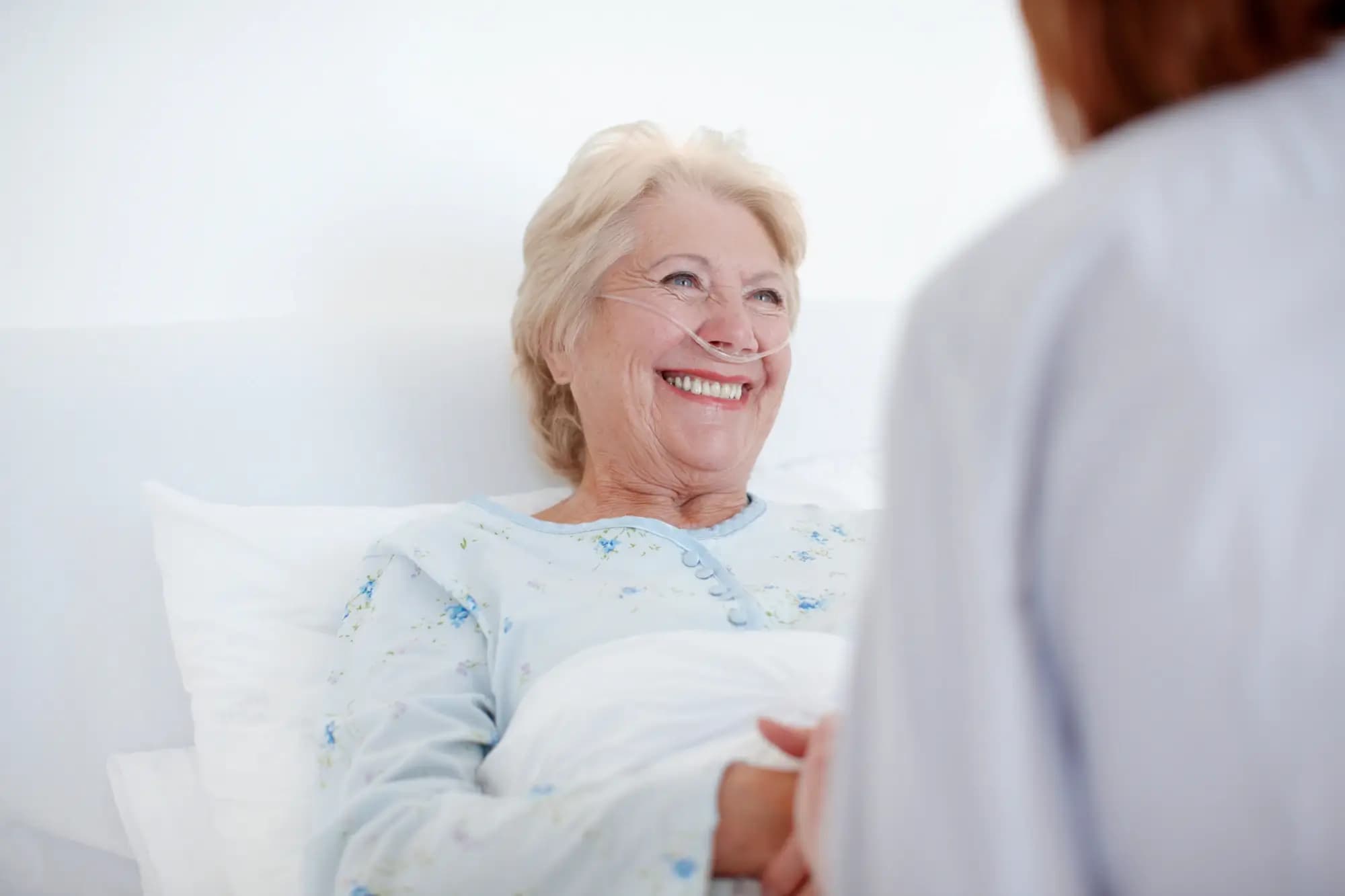 Lächelnde Patientin liegt im Bett und trägt Nasenbrille Lächelnde Patientin liegt im Bett und trägt Nasenbrille