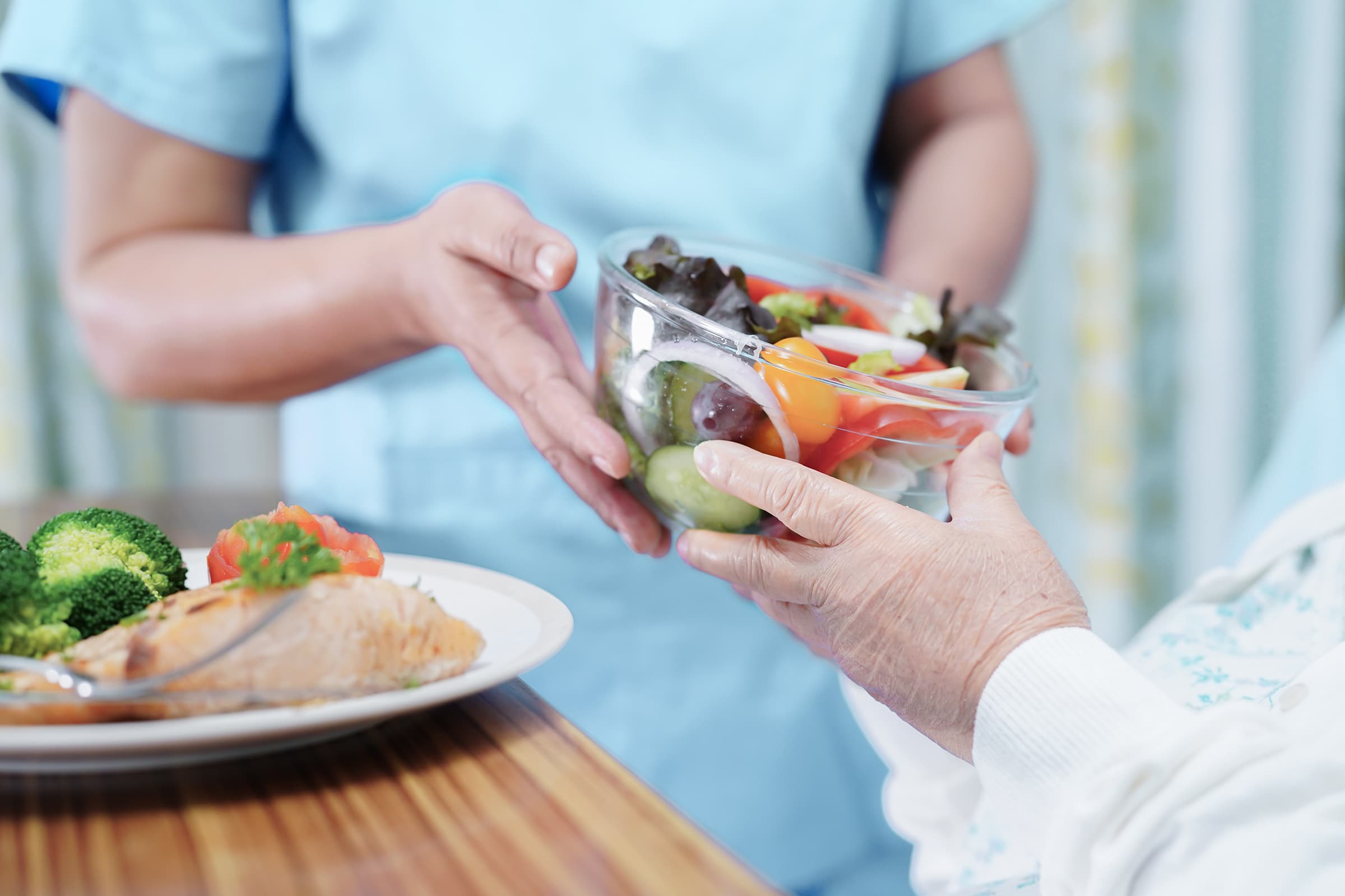 Eine Pflegekraft überreicht einem Patienten eine Schale mit Salat und frischem Gemüse Eine Pflegekraft überreicht einem Patienten eine Schale mit Salat und frischem Gemüse