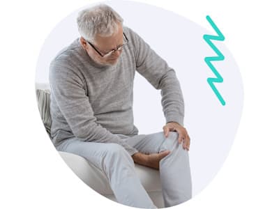 Mann, der sich aufgrund von Schmerzen mit beiden Händen an sein Knie fasst Mann, der sich aufgrund von Schmerzen mit beiden Händen an sein Knie fasst